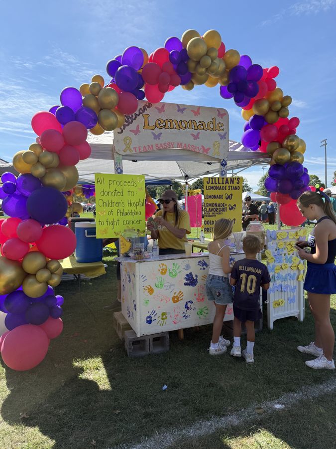 Kids at a lemonade stand under a colorful balloon arch at Community Day 2026