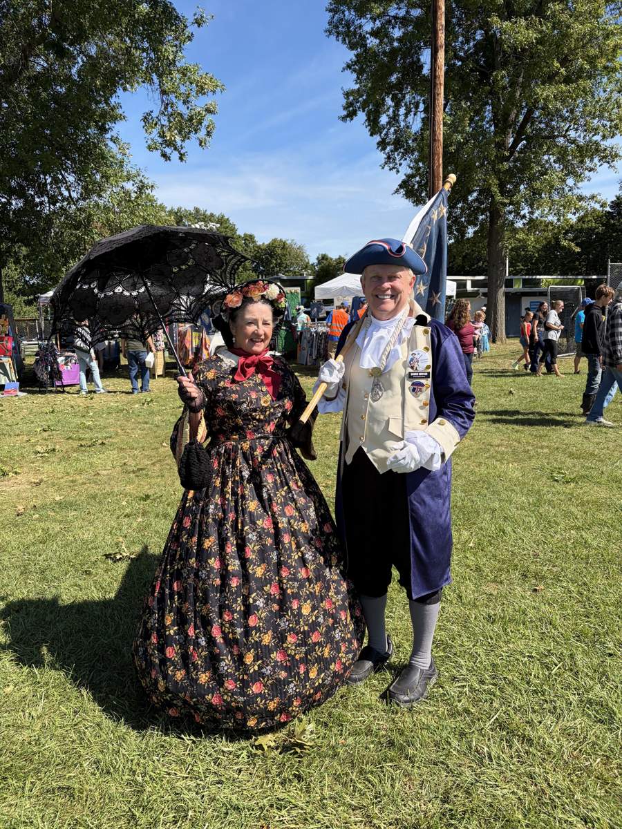 Living history reenactors in period dress, a Revolutionary War patriot carrying a flag and Mrs. Mary Todd Lincoln, at Community Day 2026